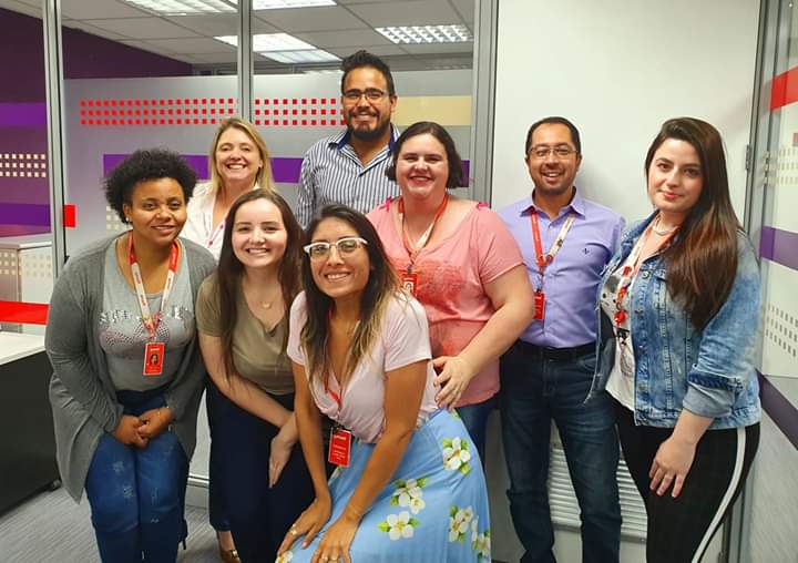 Foto tirada no interior da Getnet, com homens e mulheres, colaboradores e gestores da empresa Getnet, alguns em pé, outros agachados, ao lado da Evelyn.